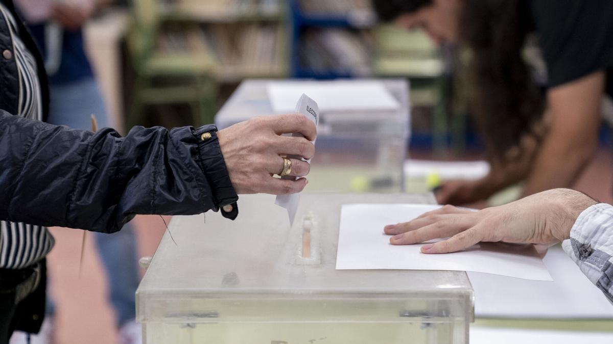 Una persona mete su voto en la urna en un colegio electoral.