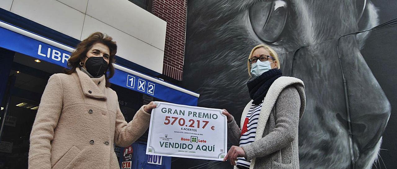 Por la izquierda, Cándida Jorge y María José García, ayer, delante de la administración de lotería de Lugones, con el graffiti del gato negro detrás. | A. I.