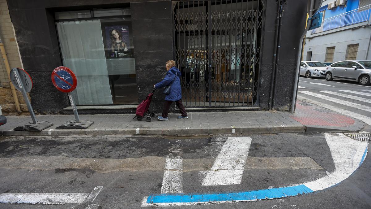 Una señora pasa junto a un comercio cerrado. En el suelo, se puede apreciar la zona azul que no llegó a implantarse.