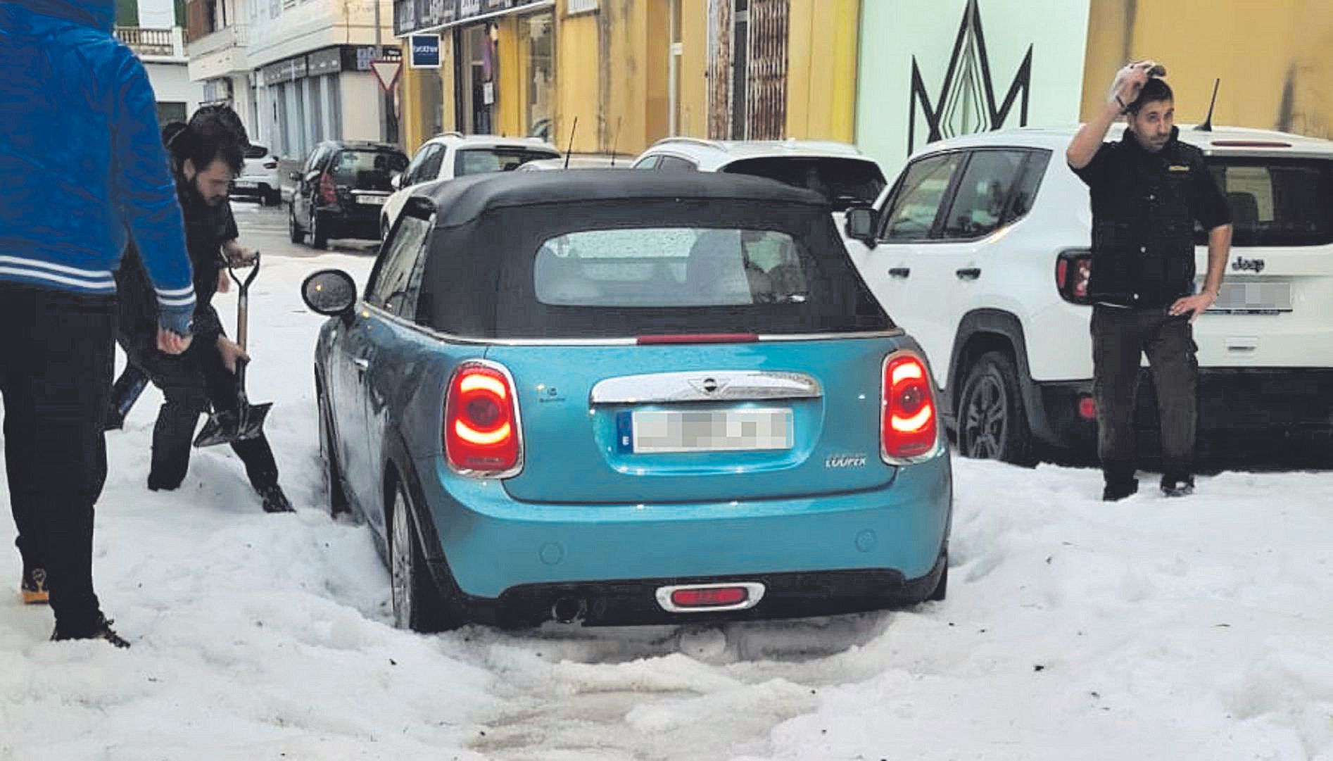 Un hombre retira granizo con una pala para liberar el coche.