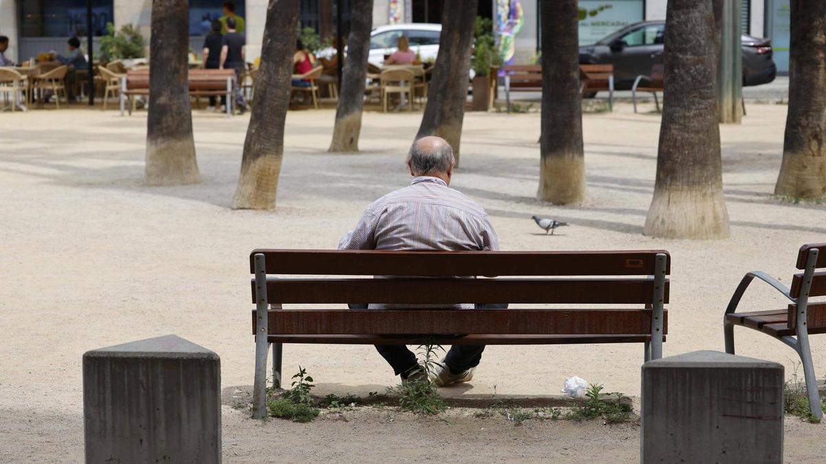 Una persona major asseguda en un banc a Girona.