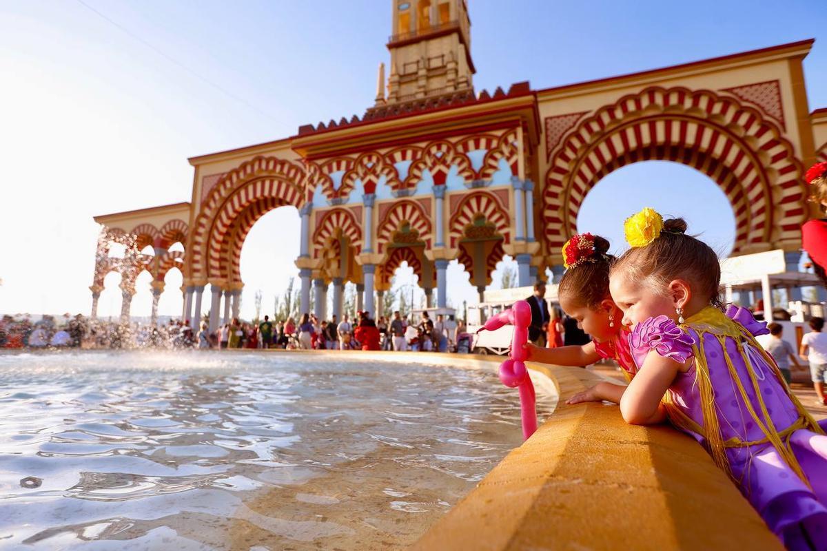 Dos niñas juegan en la fuente que hay al lado de la portada de la Feria.