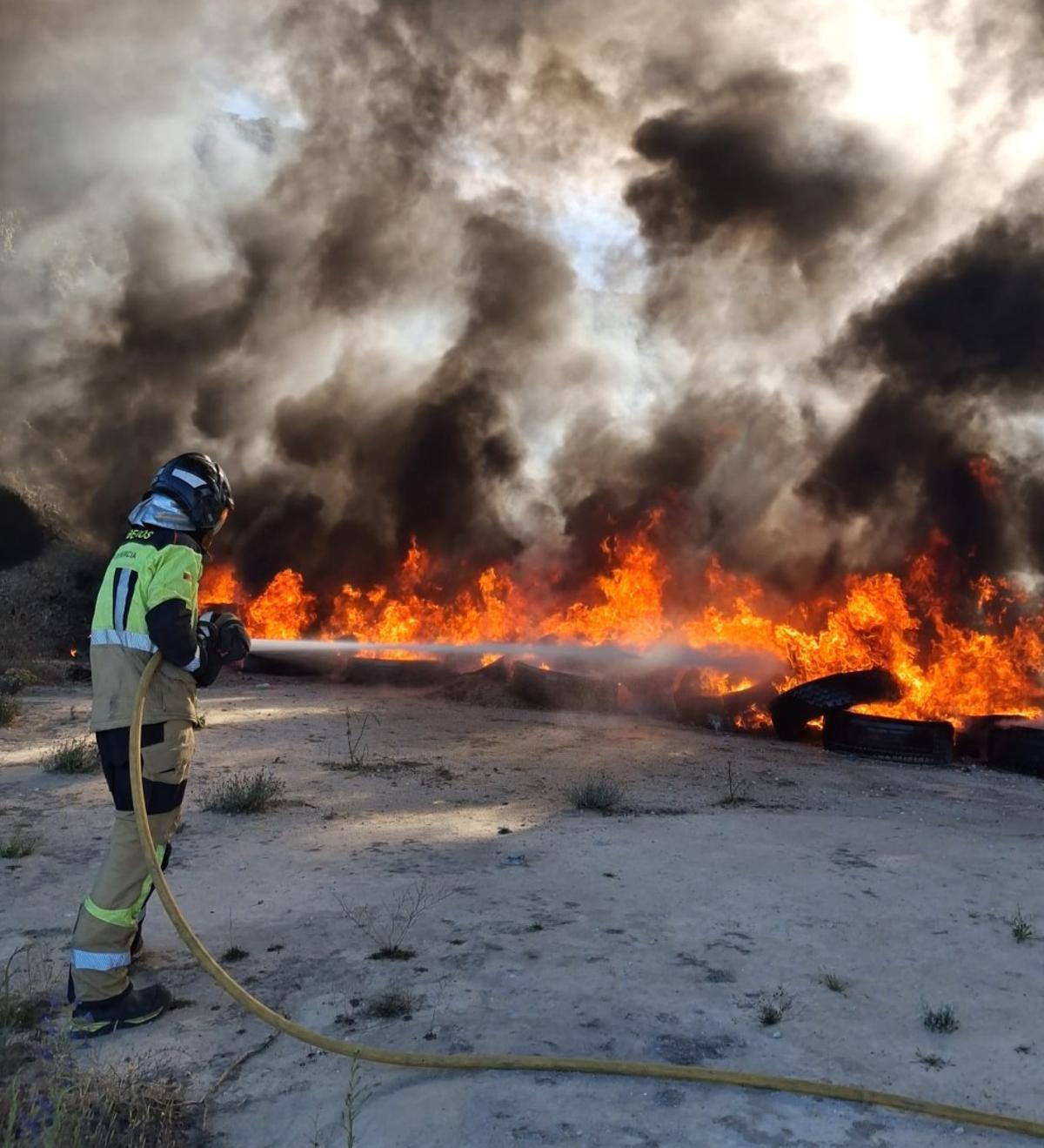 Un bombero extiende las llamas que salen de unos neumáticos