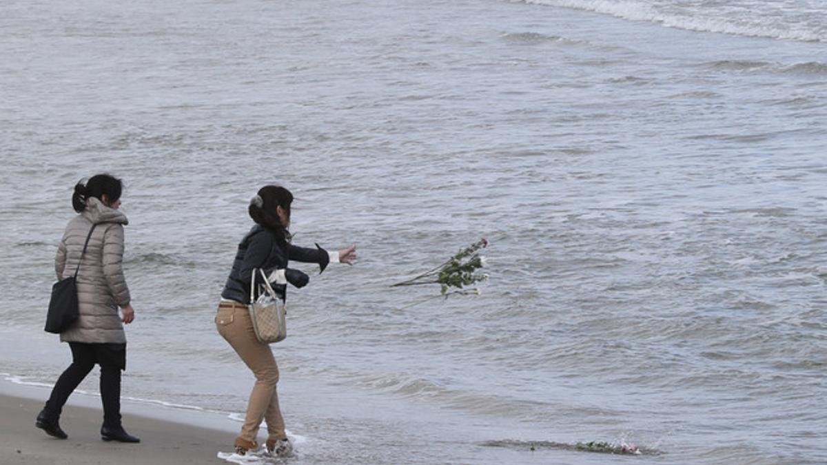 Dos mujeres lanzan flores al mar en memoria de las víctimas del tsunami.