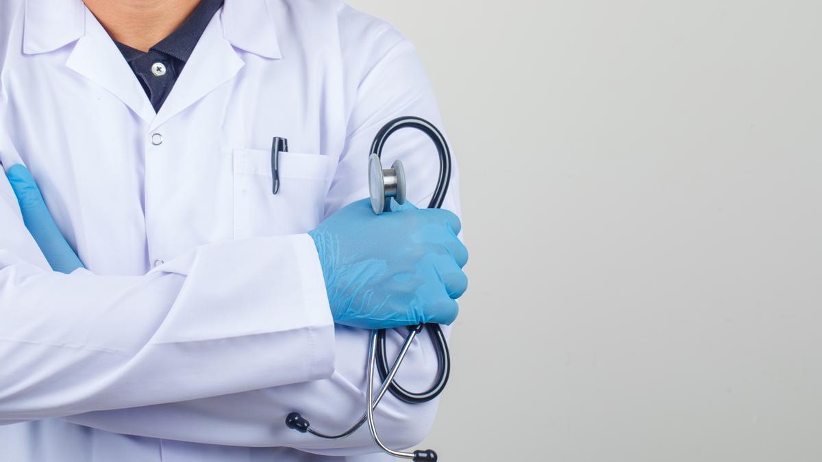 Doctor crossing arms while holding stethoscope in white coat front view.