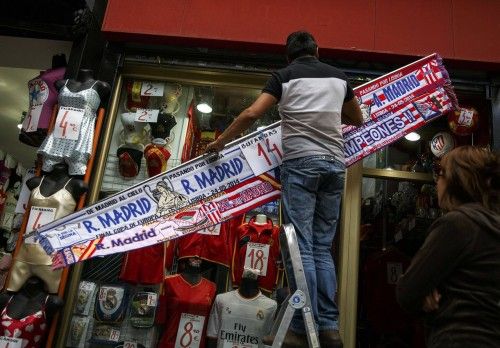 A man hangs Real Madrid and Atletico Madrid scarves outside a souvenir shop in central Madrid