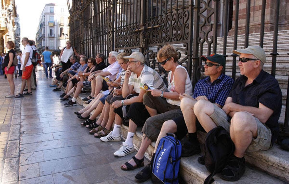 Un grupo de turistas descansa junto a la entrada de la Catedral de Málaga.