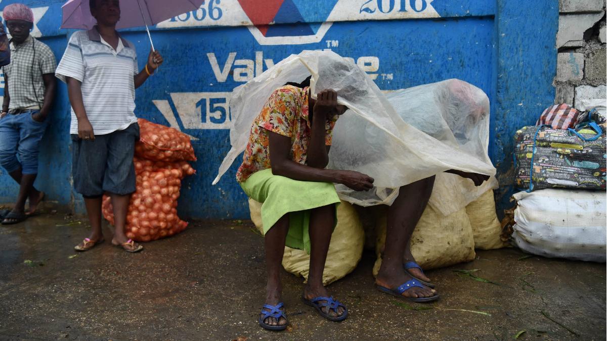 Unas mujeres se protegen de la lluvia con un plástico en la capital de Haití, Port-au-Prince.