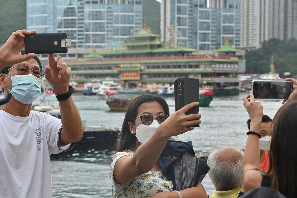 Diversas personas se toman fotos con el restaurante Jumbo de fondo, antes de que sea remolcado fuera del puerto tras cerrar sus puertas.