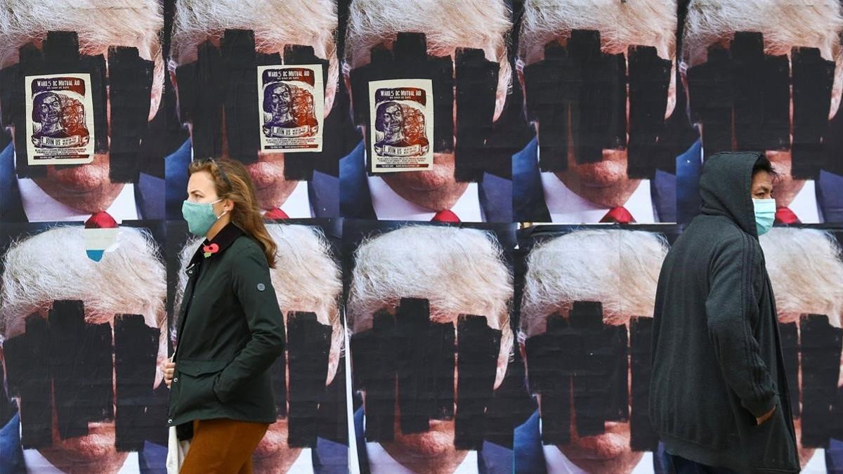 Dos personas caminan ante carteles de Donald Trump tachados, este viernes en Washington.