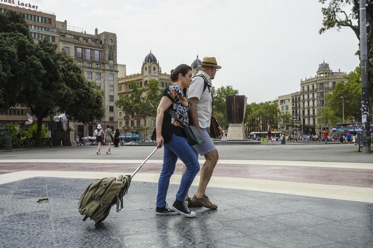 Una pareja de pasea con sus maletas por Plaza Catalunya