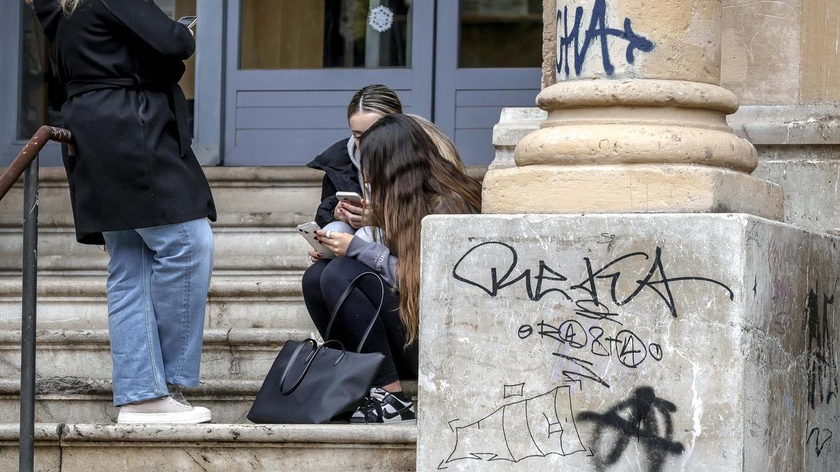 Varias jóvenes consultan su teléfono móvil a la salida de un instituto en Palma.