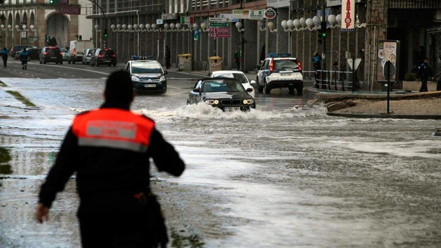 Varios vehículos circulan por una calle de A Coruña que se encuentra inundada tras sobrepasar las olas el paseo marítimo de la ciudad.