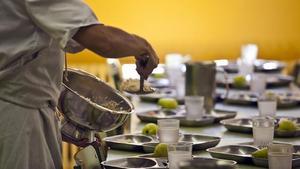 Una monitora del comedor escolar llena las bandejas de los alumnos.