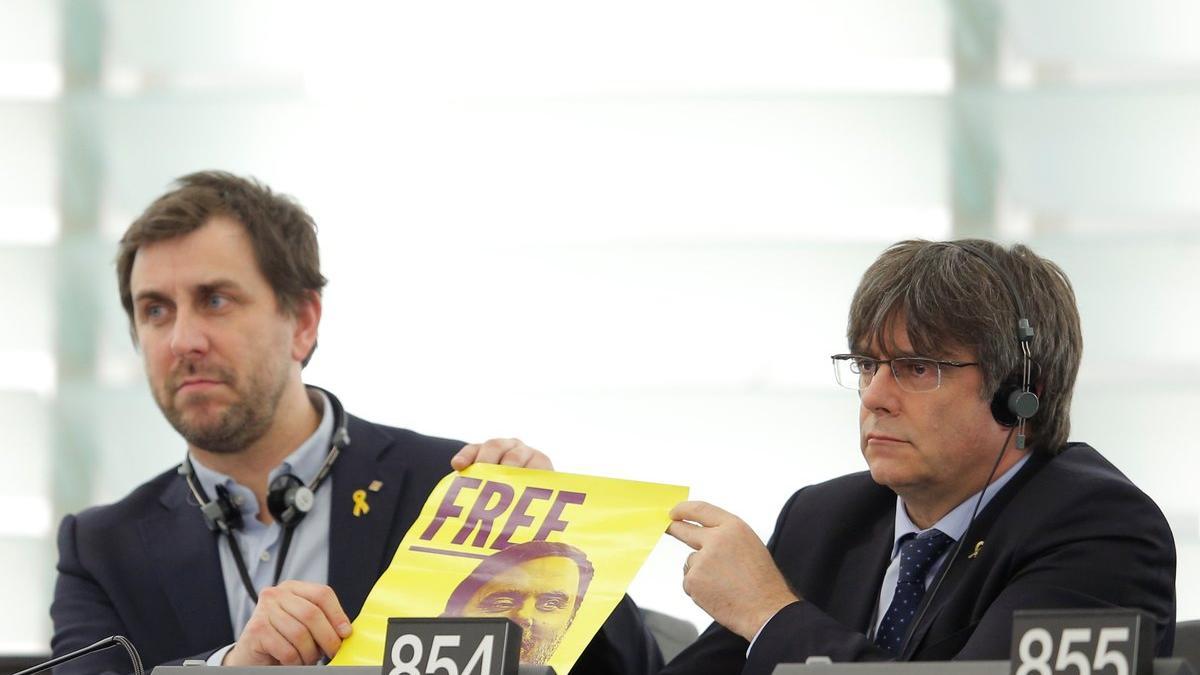 Toni Comín y Carles Puigdemont muestran un cartel de Junqueras en sus escaños del Parlamento Europeo, este lunes.