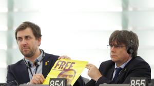 Toni Comín y Carles Puigdemont muestran un cartel de Junqueras en sus escaños del Parlamento Europeo, este lunes.