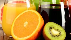 Media naranja y medio kiwi, dos frutas ricas en vitamina C, delante de unos zumos de frutas.