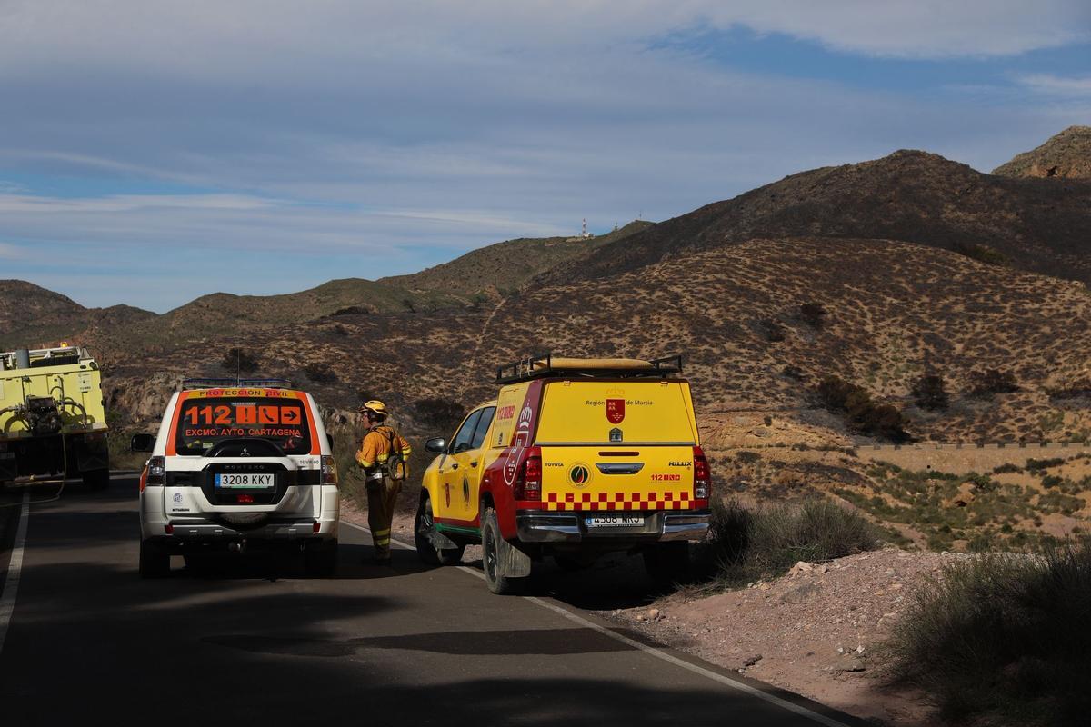 Un miembro del cuerpo de emergencias junto a varios vehículos en una zona cercana al incendio.