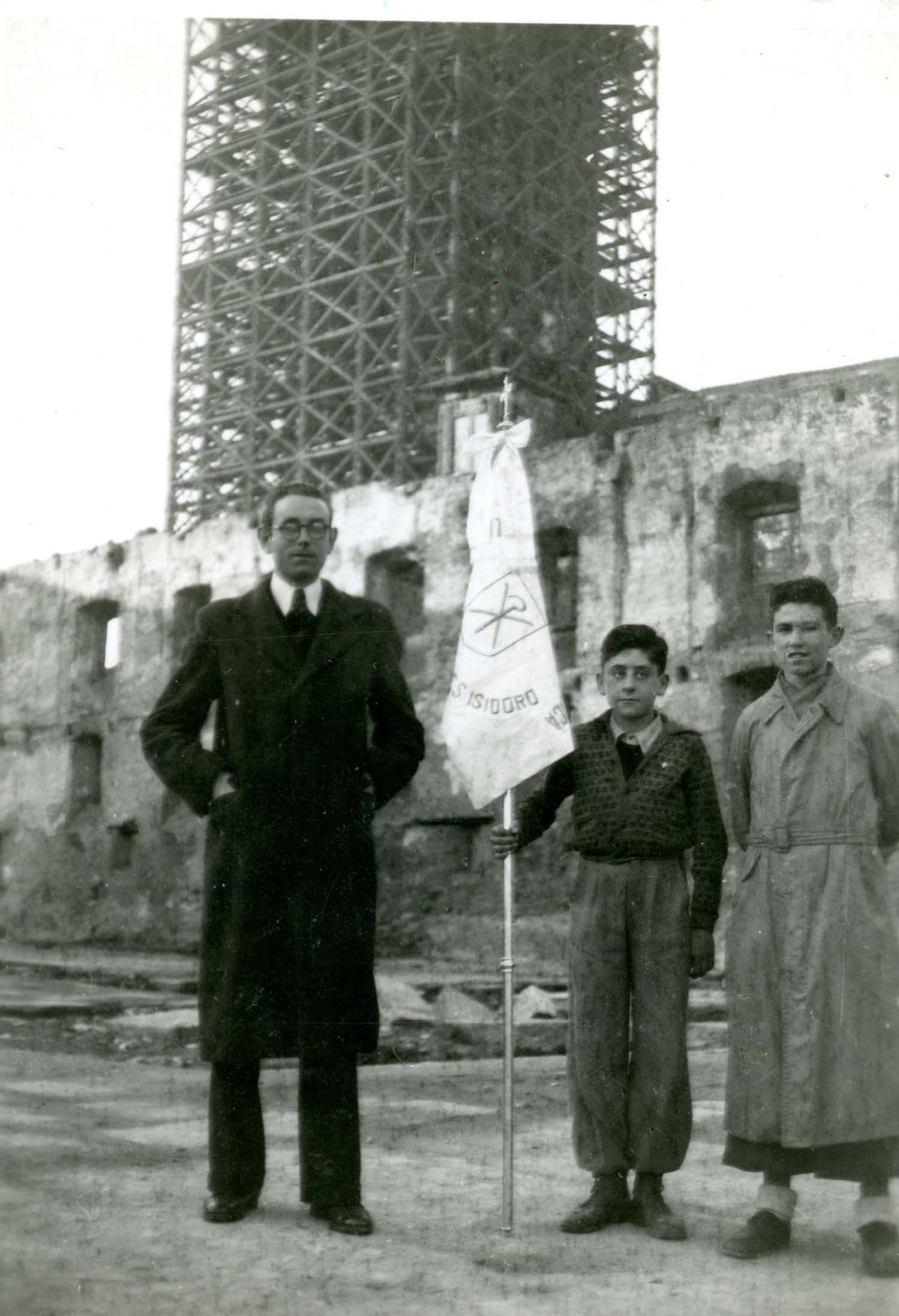 Bendición del banderín de los aspirantes de Juventud de Acción Católica de la parroquia de San Isidoro, Oviedo, en el solar del Palacio Episcopal incendiado durante la Revolución de Octubre de 1934. Al fondo, la torre de la Catedral de Oviedo andamiada para su reconstrucción, 6/1/1944 | Donación María Luisa López Llano