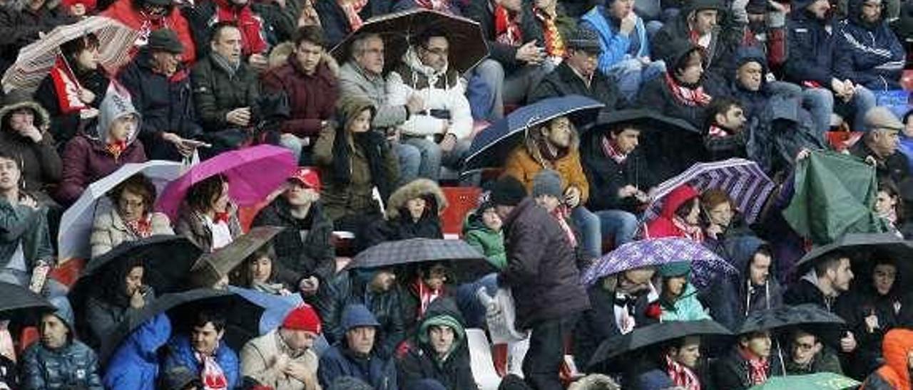 A la izquierda, paraguas y chubasqueros en la grada; a la derecha, los futbolistas durante el minuto de silencio por Gaspar Rosety y la abuela de Mascarell.