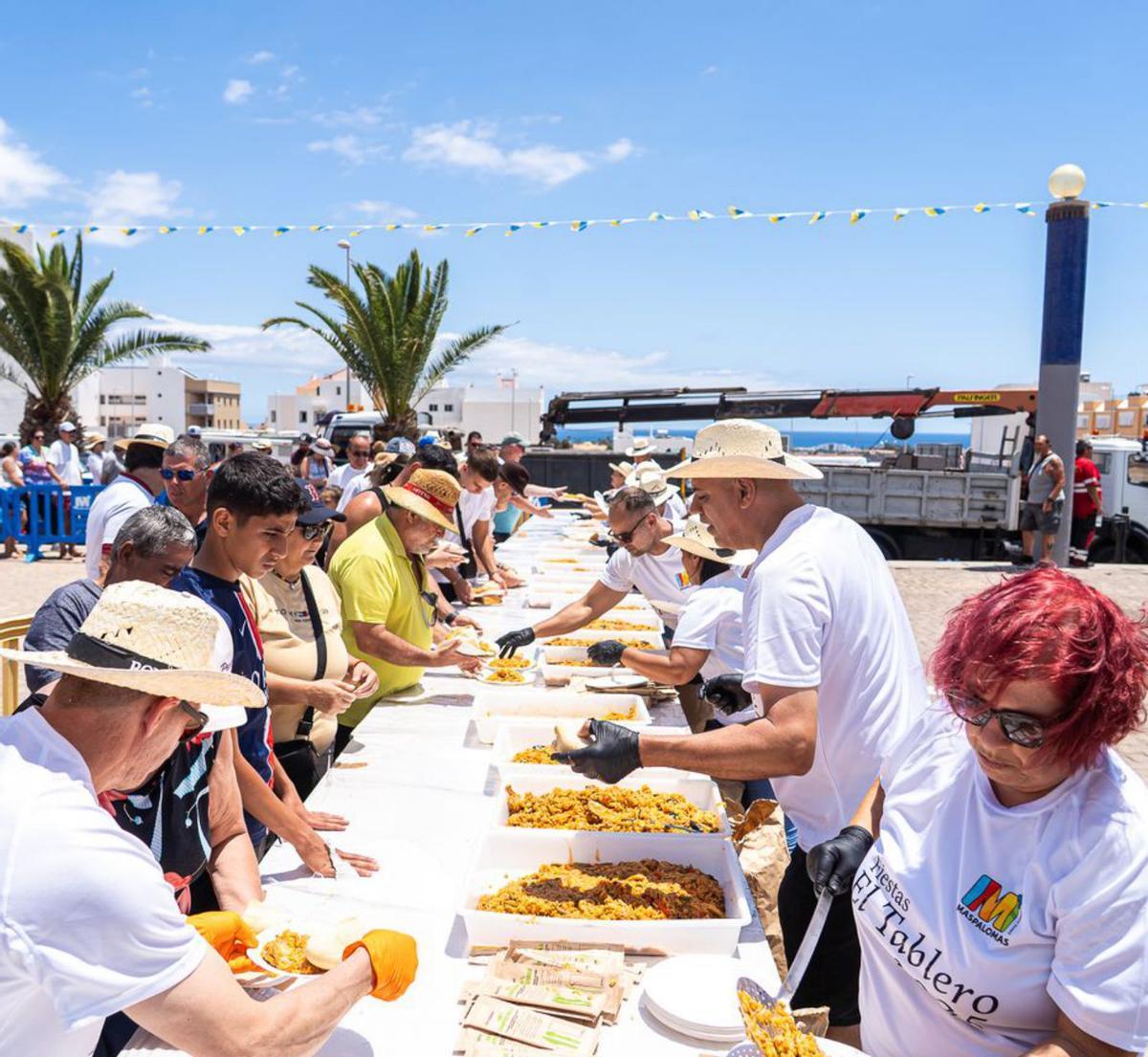 Los voluntarios reparten las raciones de la gran paella entre los asistentes en El Tablero