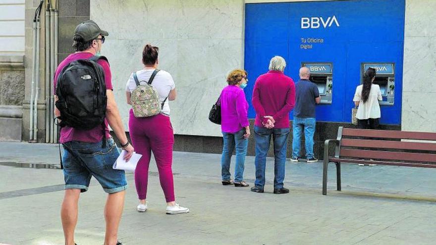 Varias personas hacen cola ante los cajeros automáticos de una sucursal bancaria.