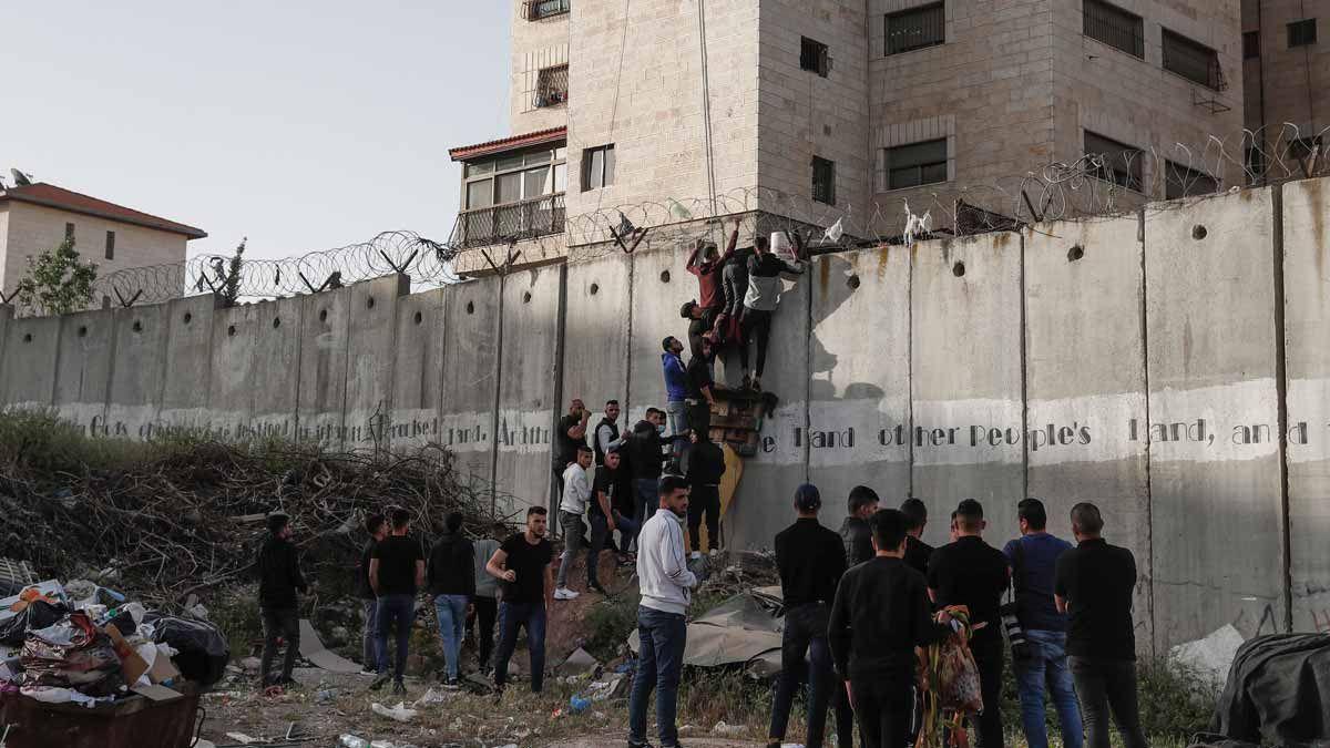 Palestinos intentando saltar el muro que separa el pueblo de A-Ram de Jerusalén para acceder a la Explanada de las Mezquitas en el último viernes de Ramadán.