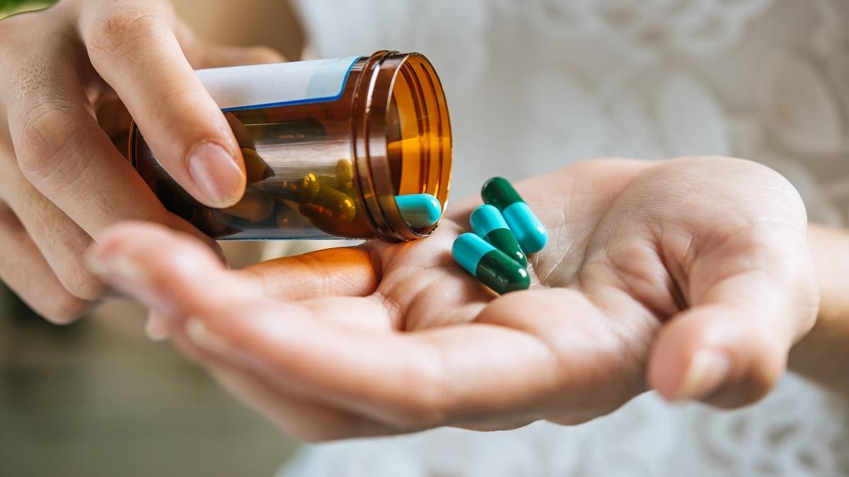 Una persona coge varias pastillas de un bote de medicamentos.