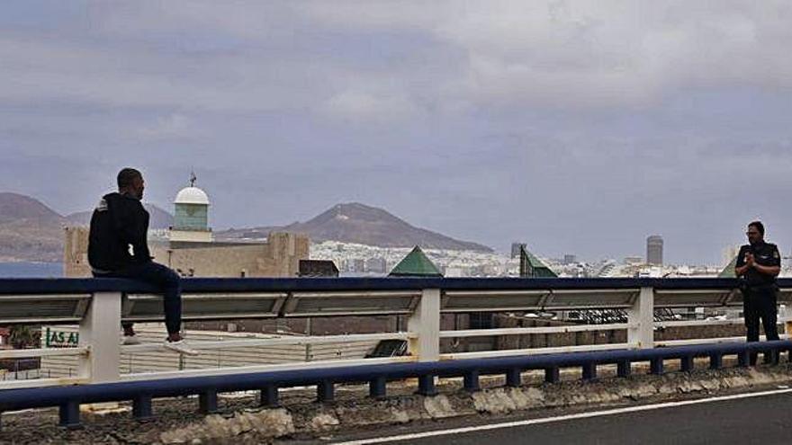 El hombre sentado ayer al borde del abismo en el viaducto de El Rincón, mientras el funcionario de la Policía Nacional intenta persuadirle para que se retire.