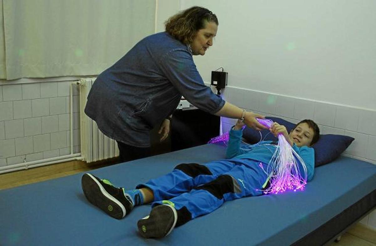 Un dels nens, usuari del centre, provant el llit musical del nou espai, acompanyat de Rosa Serrano