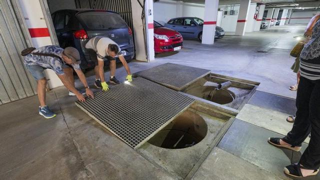 Dos de los residentes destapan dos sumideros de agua en uno de los garajes de la comunidad de vecinos.