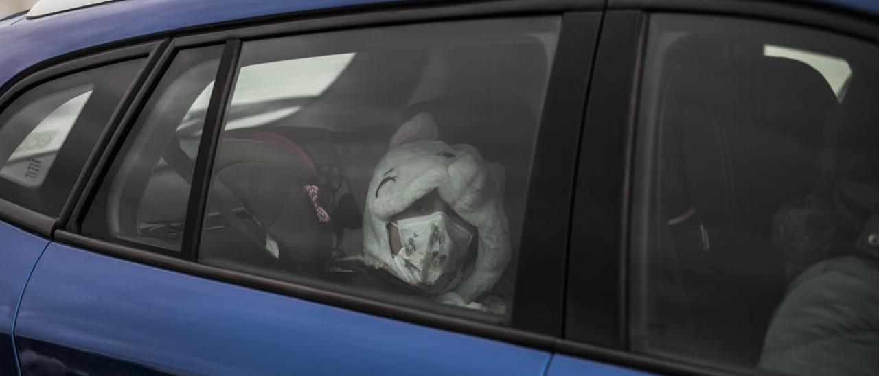 Una niña viaja en mascarilla en un coche con sus padres.