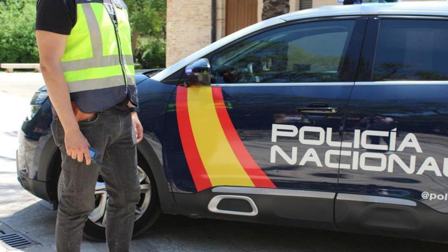 Policía de paisano (aunque con chaleco identificativo) junto a un coche potrulla.