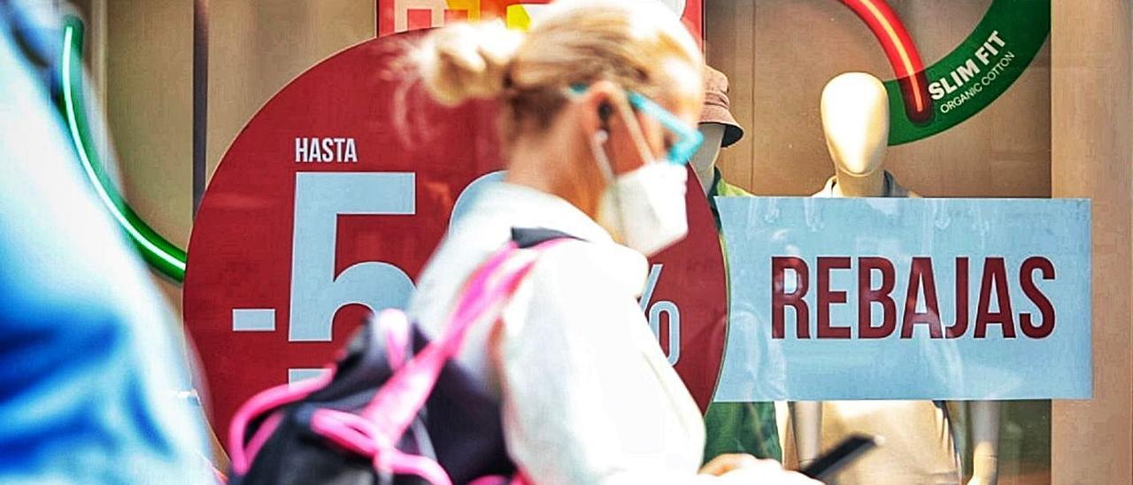 Una mujer pasea frente a un escaparate con descuentos.