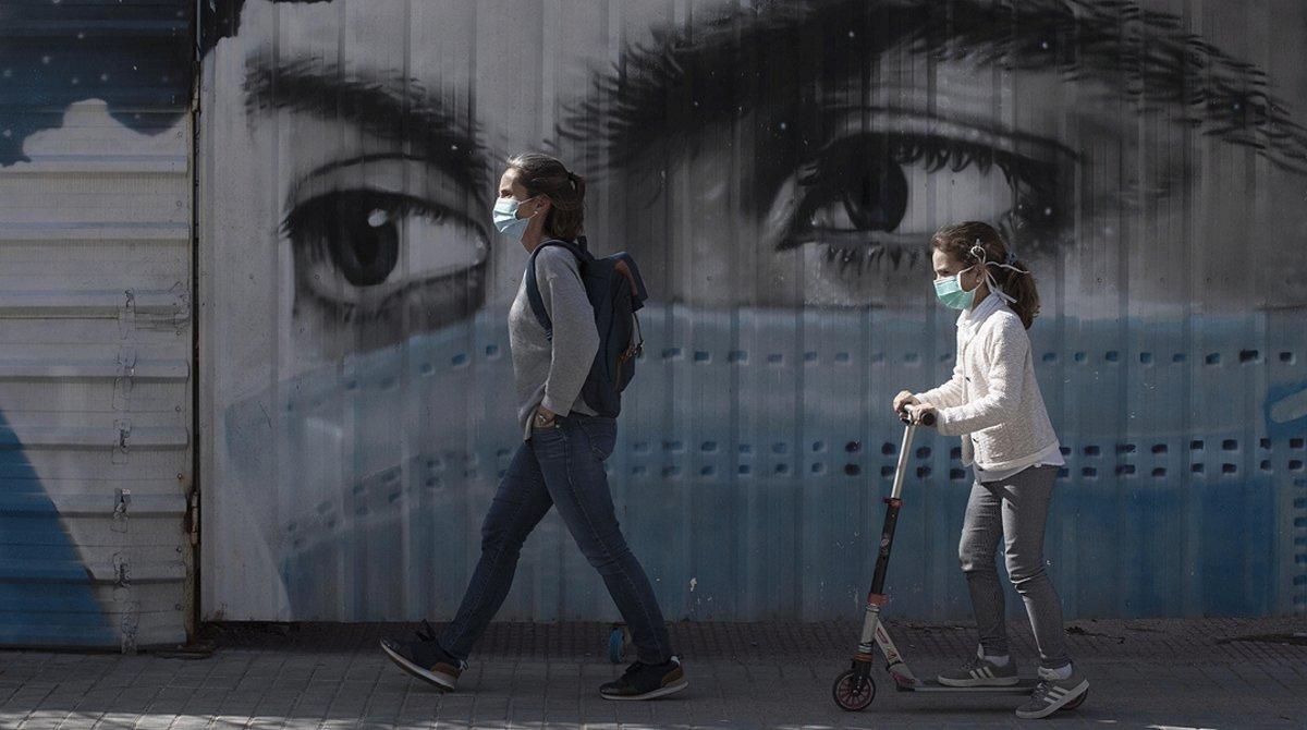 Una mujer y su hija pasean junto al grafiti de una joven con mascarilla, en Barcelona, el 28 de abril. 