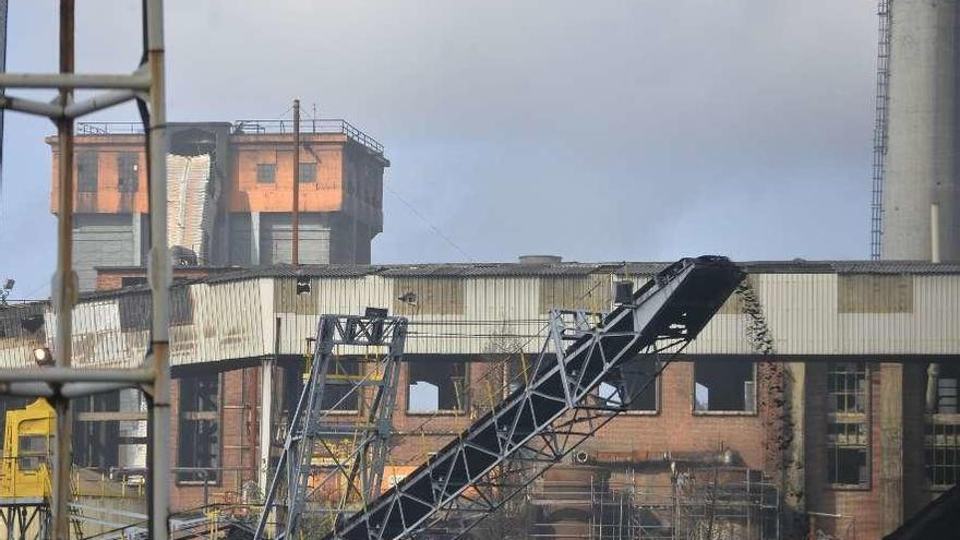 Una cinta transportadora móvil vierte coque en una pila; al fondo, la torre que distribuye carbón al primer grupo de baterías que se vio más afectada por el fuego del mes pasado, con la galería inutilizada por las llamas.