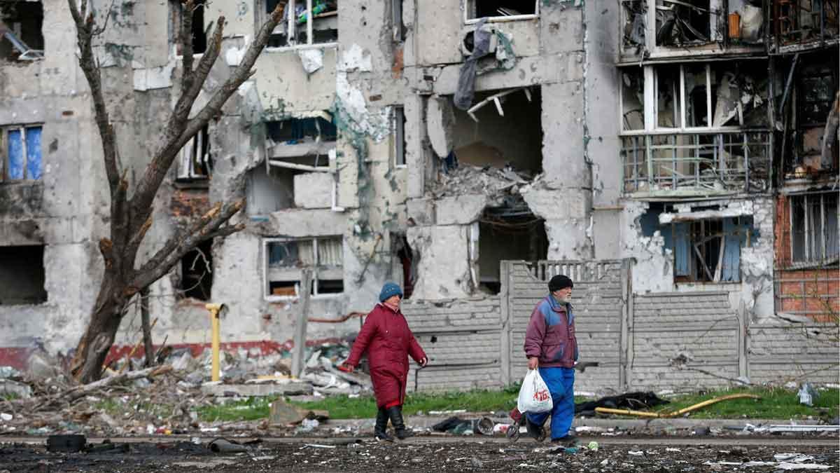 Dos personas pasan junto a un edificio de casas destruido, en la ciudad de Mariúpol