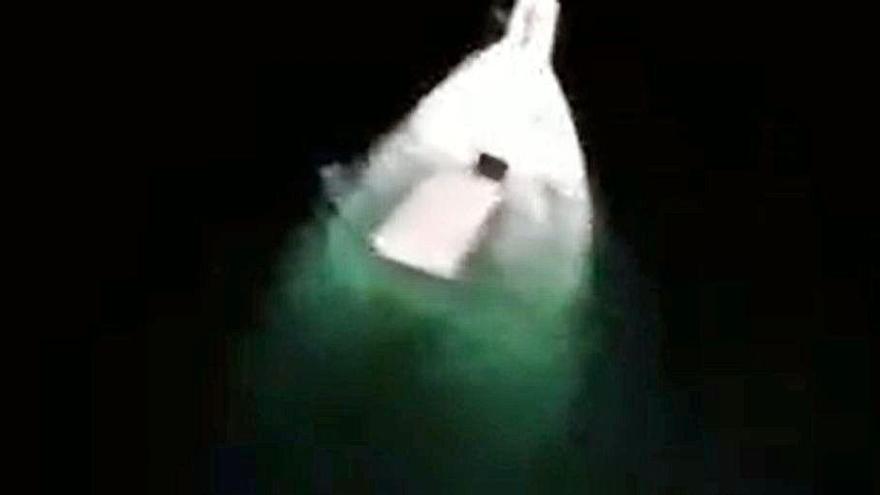 Arriba, captura de la grabación del rescate desde el helicóptero de Guardacostas Pesca I y a la izda., la lancha semihundida.