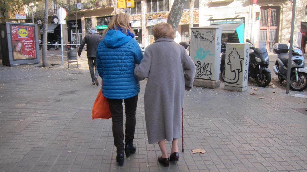 Una mujer pasea con su cuidadora por una calle.