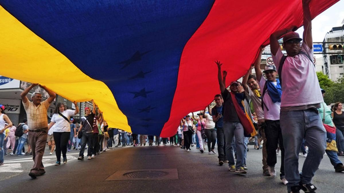 Un grupo de ciudadanos porta una bandera venezolana gigante, este domingo en Caracas, durante la marcha contra el Gobierno.