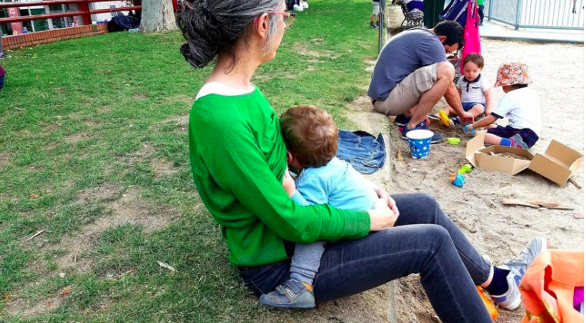 Una madre da el pecho a su bebé en un parque.