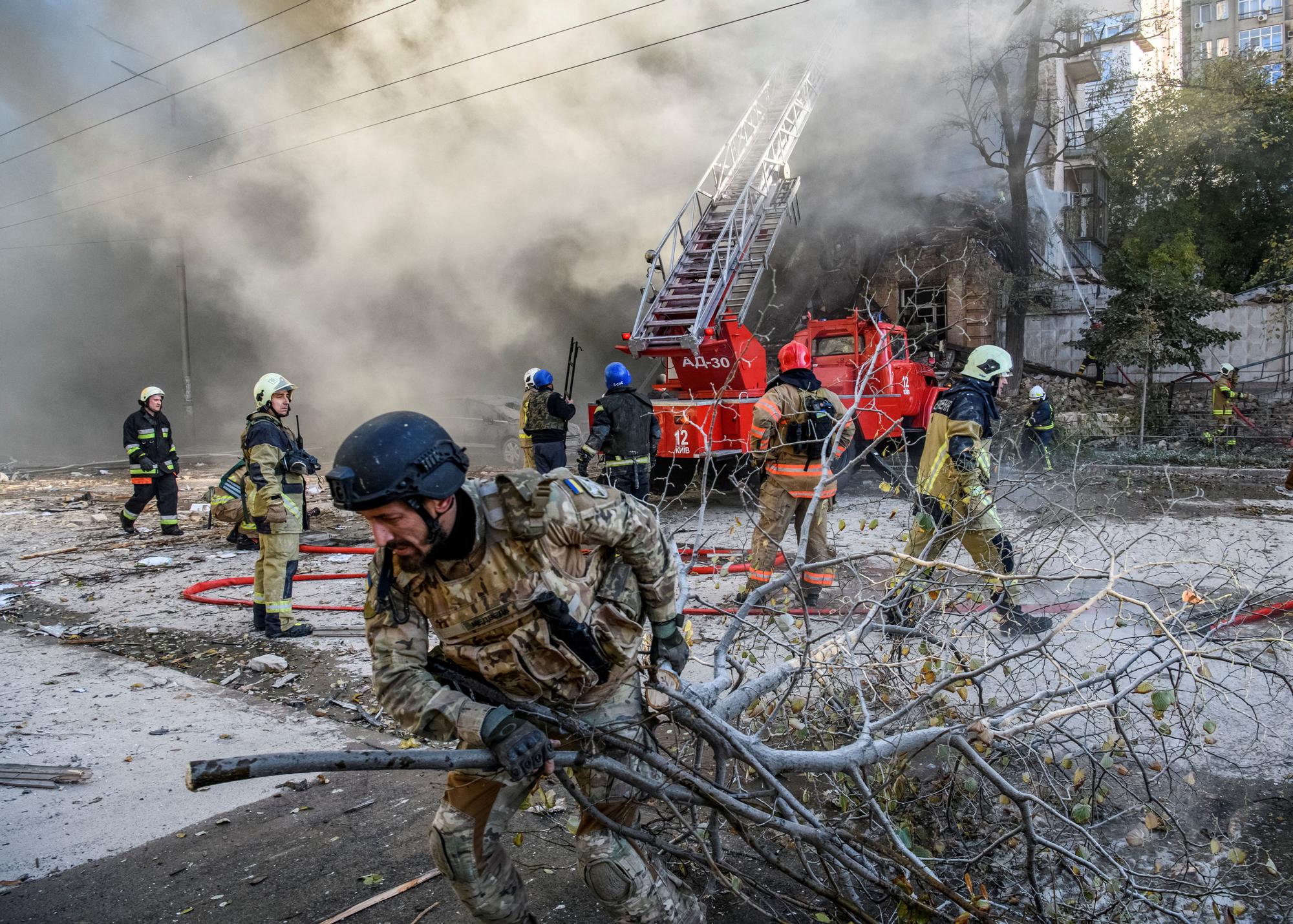 Bomberos ucranianos ayudan a evacuar un edificio en llamas en Kiev.