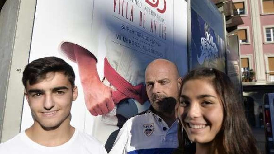 Carlos Fernández, en el centro, presidente del Club Judo Avilés, con los judocas Javier Corral y Alba Barreiro junto a un cartel del Villa de Avilés.