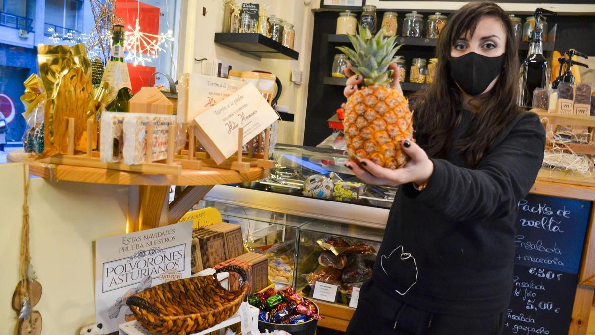 Sofía González Vara, propietaria de Eliso Alimentación en Oviedo, muestra una piña junto varios productos navideños, en su establecimiento