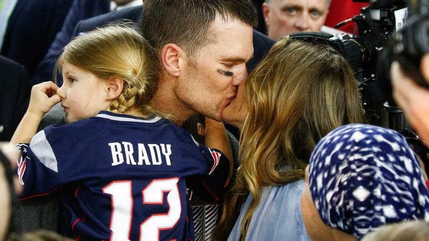 Tom Brady, con su hija, Vivian en los brazos, besa a su mujer, Gisele Bündchen.