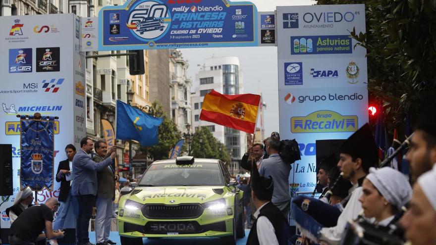 Adrián Barbón y Julían Moreno, con la bandera de Astuy, conrias, dan la salida al rall Manuel Aviñó, presidente de la Federación Española de automovilismo, debajo de la bandera de España.