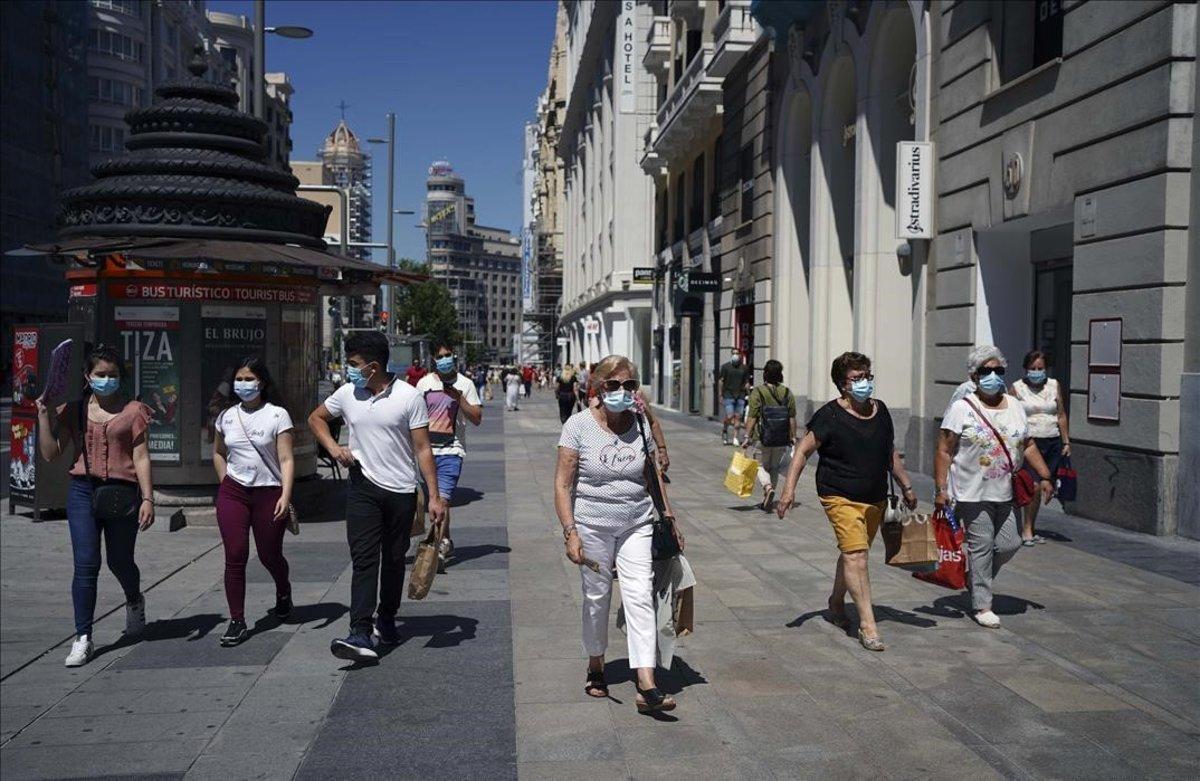 Gente con mascarillas en la denominada nueva normalidad pasea por la Calle Gran Vía de Madrid .