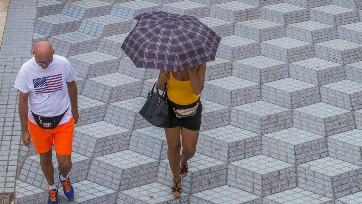 Una mujer se protege de la lluvia con un paraguas mientras pasea junto a la playa.