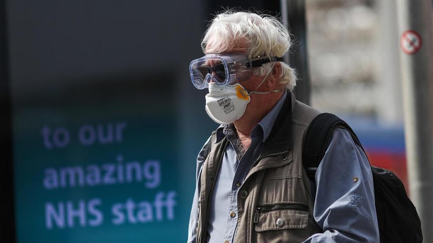 Un viajero con una máscara facial protectora, gafas y guantes camina en la estación de tren de Waterloo en Londres.