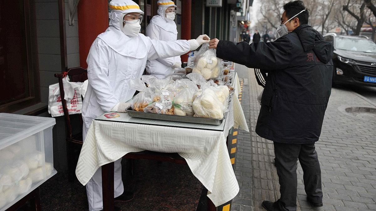 Un trabajador de un restaurante, vestido con ropa protectora, entrega a un cliente su menú, en una calle de Pekín